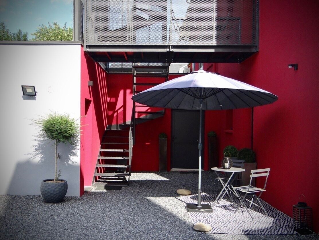 A red and white building with a small patio area featuring a table, chairs, and an umbrella.