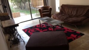 Een woonkamer met een bruine bank, een klein tafeltje en een zwart-rood tapijt met een patroon.