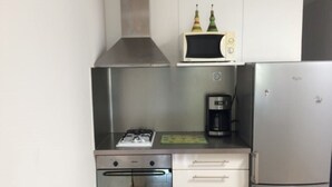 Een kleine keuken met een gasfornuis, een koffiezetapparaat, een magnetron en een koelkast.