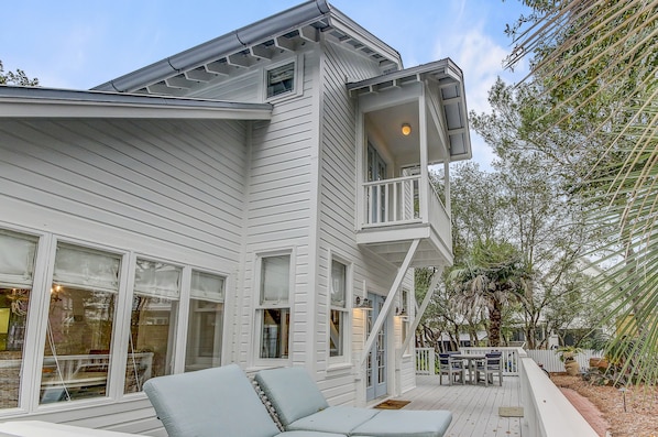 A white house with a balcony, large windows, and a deck with outdoor furniture.