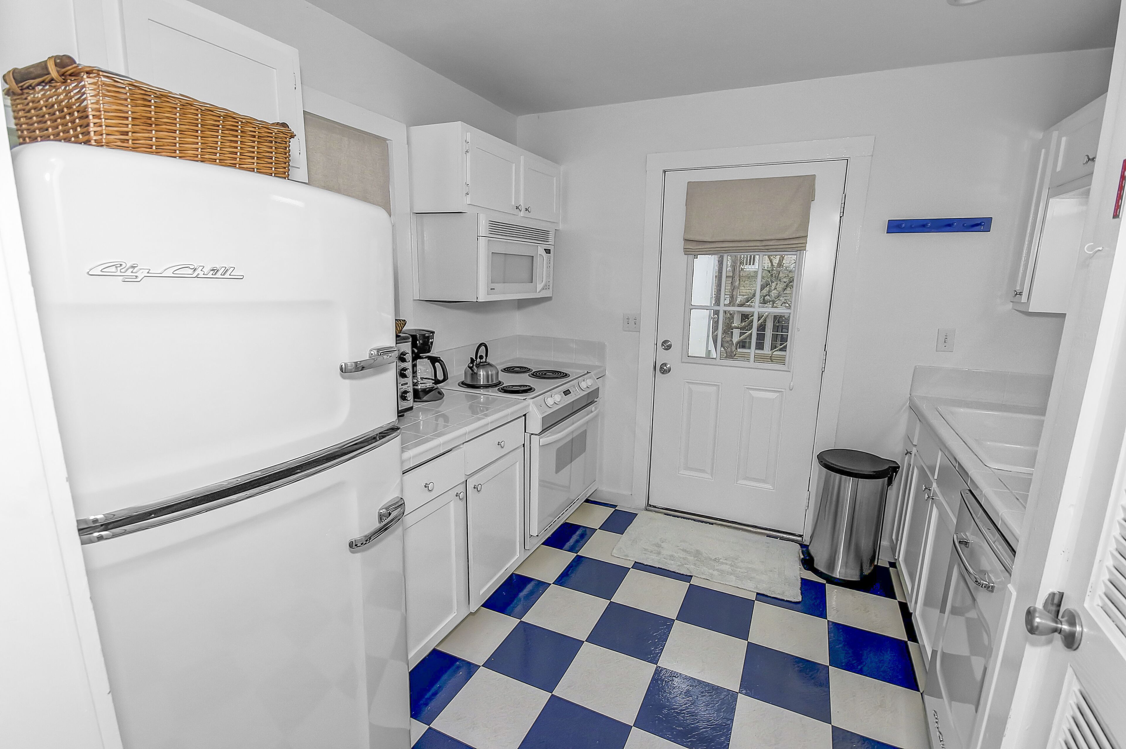 A compact kitchen with white appliances, a checkered floor, and a door with a window.
