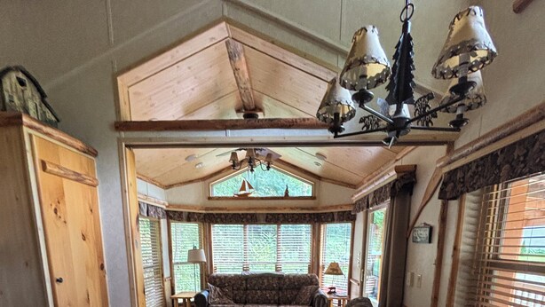 Interior acogedor de una cabaña con una mesa de comedor de madera, sillas, un sofá y un ventanal con persianas.