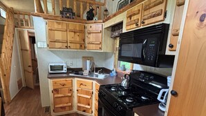 Cocina pequeña con armarios de madera, un microondas, estufa y pileta.