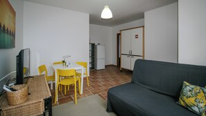 En kompakt opholdsstue med sofa, spisebord, stole, fjernsyn og et tekøkken.