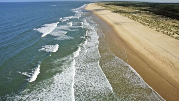 Een strand met een lange zandvlakte en golven die op het strand breken.