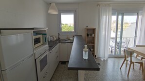 Een compacte keuken met een magnetron, oven en gootsteen. Er is een zithoek met een tafel en stoelen, en een balkon met uitzicht.