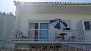 Een gebouw met een balkon, een blauw-witte parasol en twee tafels met stoelen.