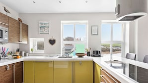 A modern kitchen with a large island, a built-in oven, and a view of the countryside. - The Penthouse, 16 At The Beach, Wi-Fi, Sea View (Kingsbridge)