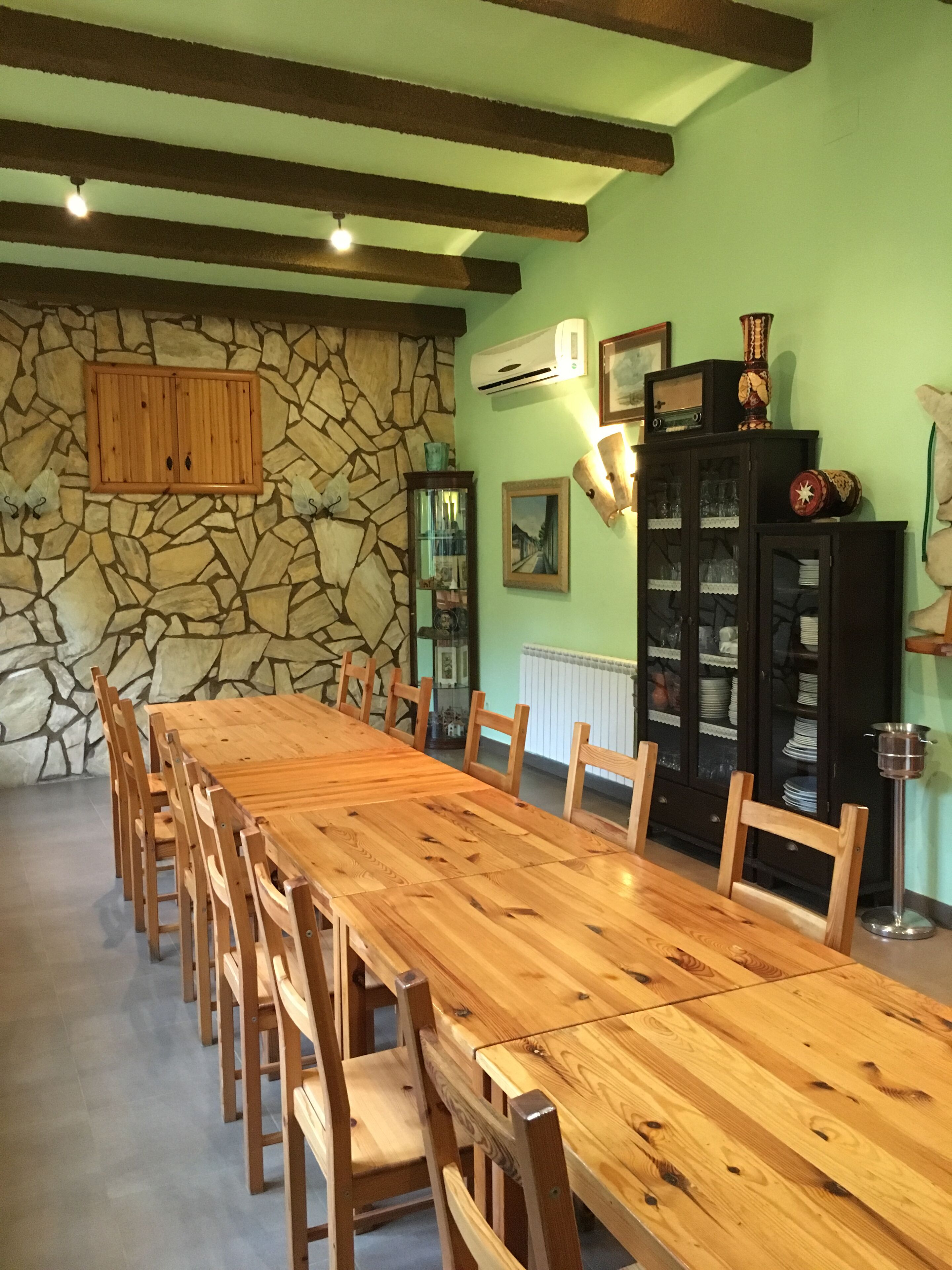 Un espace repas comprenant une longue table en bois et des chaises, un mur en pierre et un buffet aux portes vitrées.