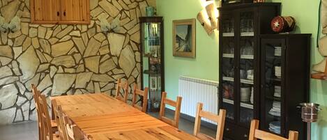 Un espace repas comprenant une longue table en bois et des chaises, un mur en pierre et un buffet aux portes vitrées.
