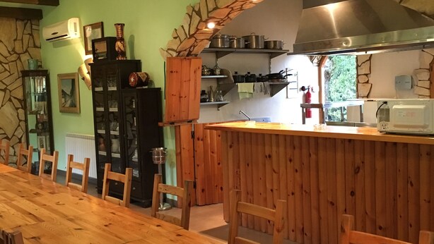 A long wooden dining table with chairs, a kitchen area with wooden cabinets and a stone arch, and a stone wall with a window. - Still available from August 17 to August 31! La Xaconera d' Ardenya (Ardenya, Tarragona)