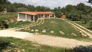 A rustic house with a red-tiled roof, surrounded by a grassy area with scattered rocks and a dirt path leading to it. - Still available from August 17 to August 31! La Xaconera d' Ardenya (Ardenya, Tarragona)