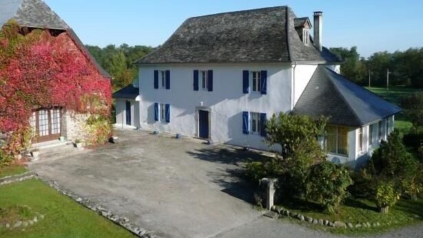Un grand bâtiment blanc avec un toit gris, une petite construction attenante avec un toit rouge et une allée pavée.