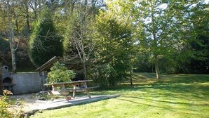 Un espace extérieur verdoyant, avec une table de pique-nique et une petite construction, le tout entouré d’arbres.