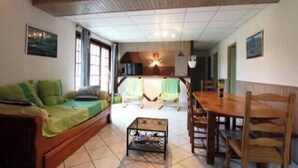 Un salon chaleureux avec un canapé, une table à manger entourée de chaises, une petite table basse et, au fond, un coin cuisine.