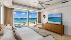 Un dormitorio con una cama grande, televisión, aparador de madera y vista al océano con barcos.