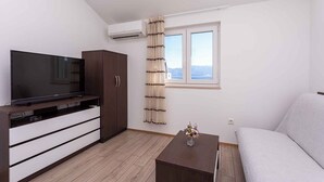Un salon moderne avec un téléviseur à écran plat, un meuble en bois, un canapé, une petite table avec un vase et une fenêtre avec des rideaux.