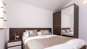 Une chambre à coucher moderne avec un grand lit, une table de chevet avec une lampe, une armoire et un miroir.