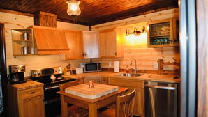 A wooden cabin kitchen with a wooden table, chairs, a microwave, a sink, and a dishwasher. - Charming cottage with pond in Heart of New River Gorge (Victor)