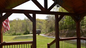 A wooden deck with a view of a pond, a small building, and a forested area. - Charming cottage with pond in Heart of New River Gorge (Victor)