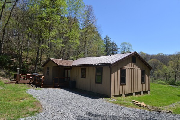 Une cabane en bois d’un seul étage, avec un toit en métal, une allée en gravier et une terrasse dotée de meubles d’extérieur.