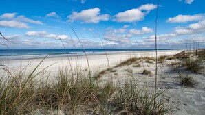 Ein Strand mit Dünen, einem Holzzaun und blauem Himmel.