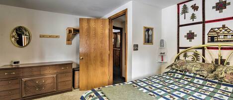 A bedroom with a bed, wooden dresser, and a door leading to another room.