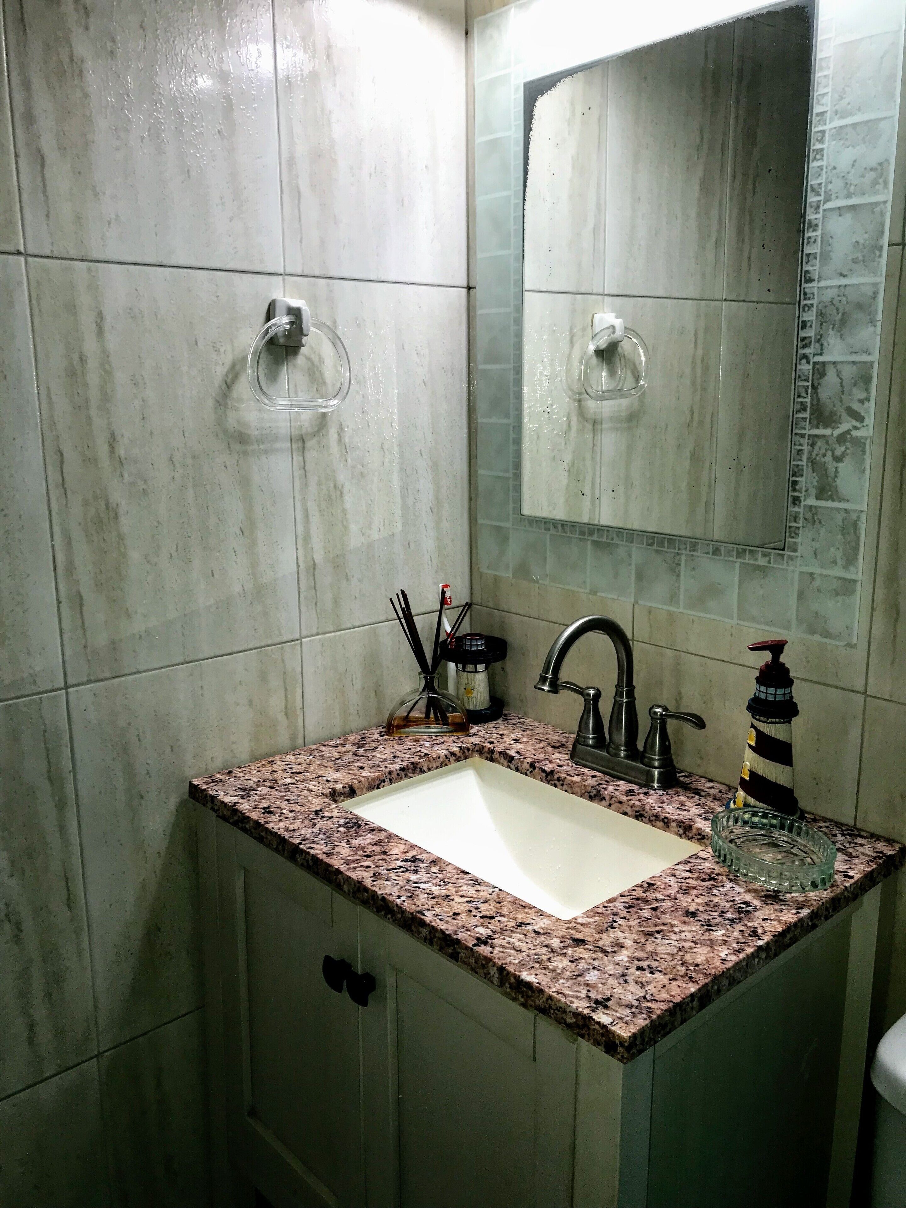 Baño con lavamanos de encimera de granito, espejo y dispensador de jabón.