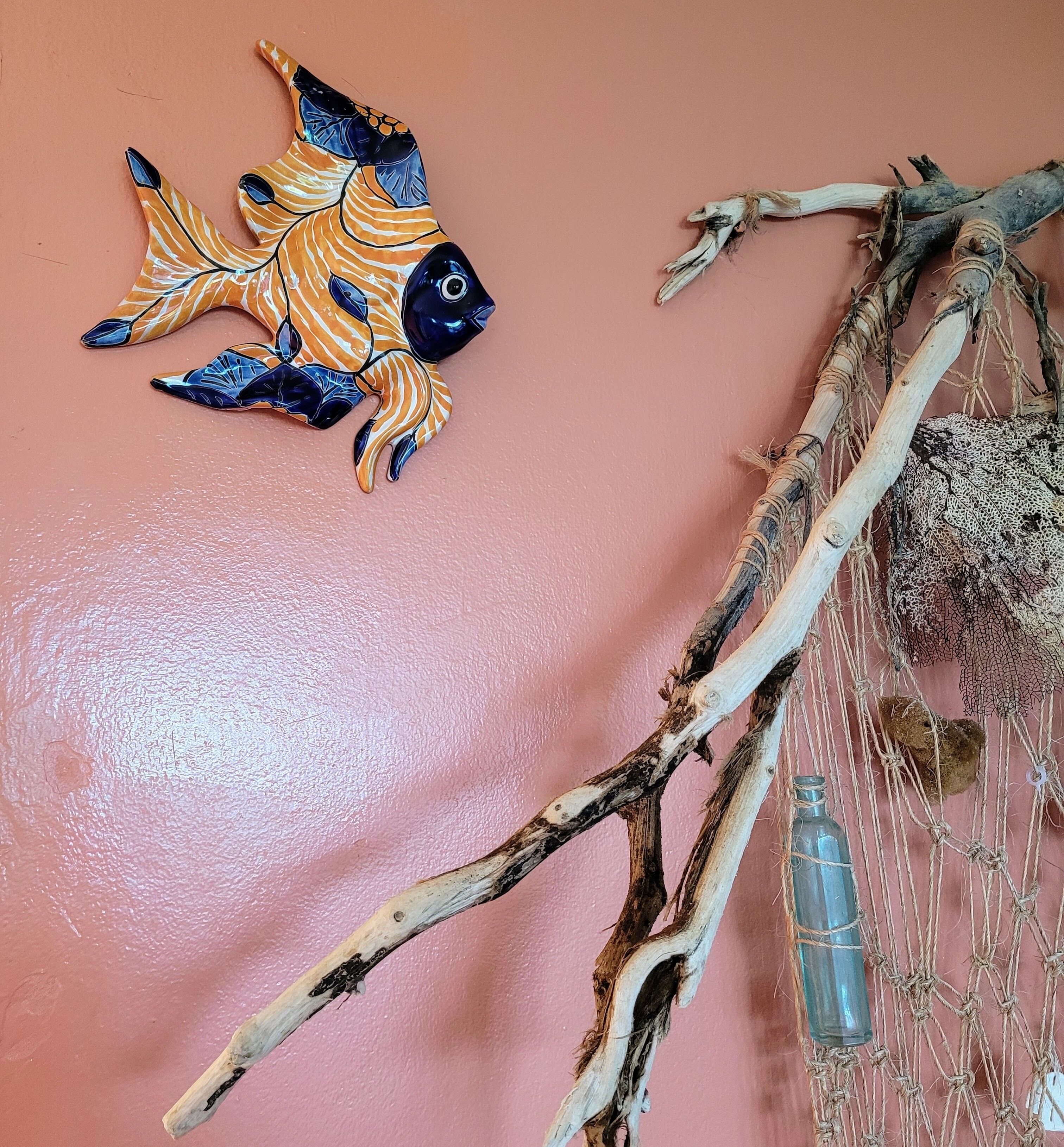 A wall with a decorative fish, a macrame piece, and a bottle.