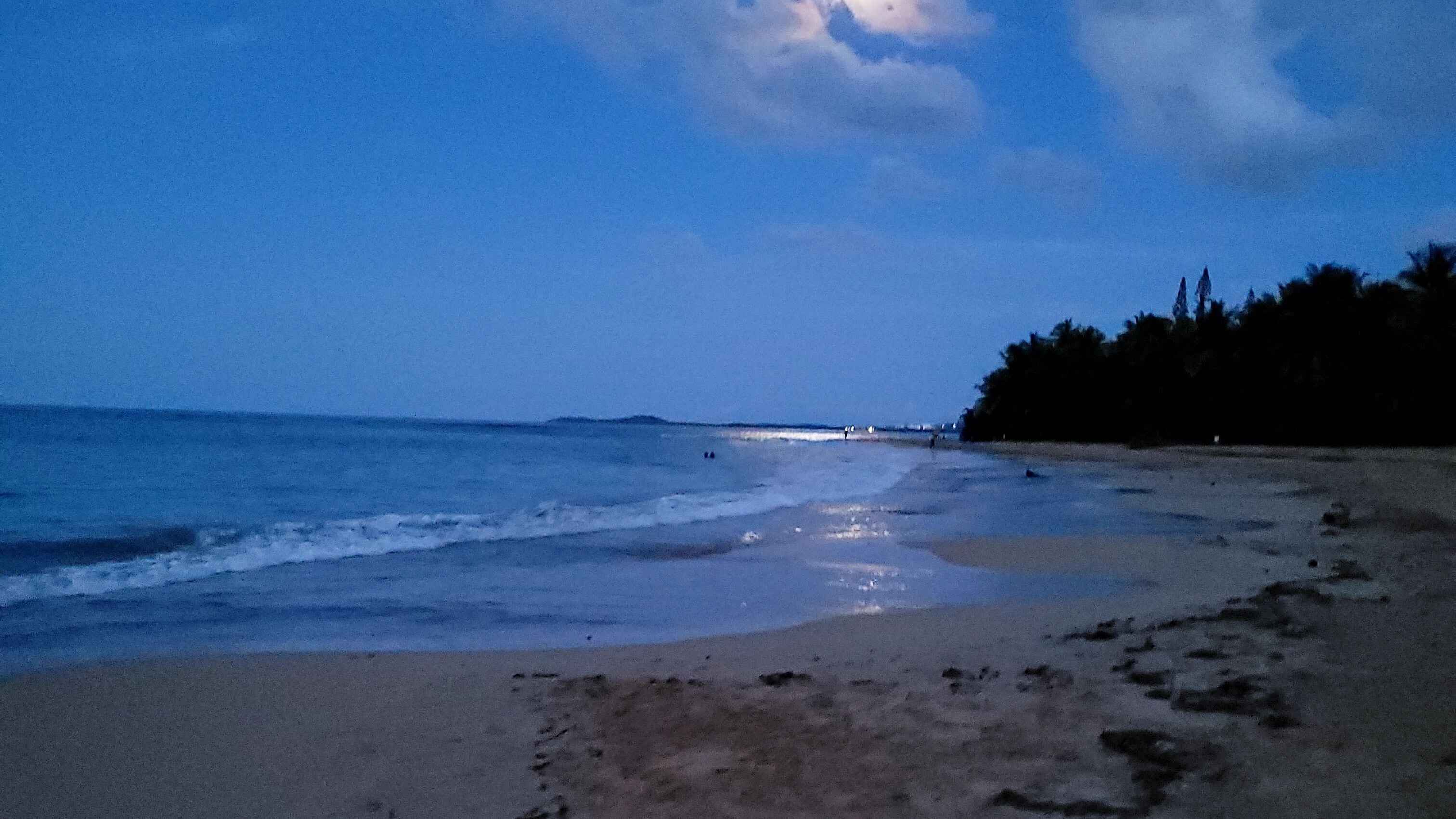 A beach with a calm sea, sandy shore, and a few footprints.