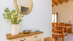Una habitación con una mesa de comedor de madera, sillas, un jarrón con flores, un espejo y un armario pequeño.