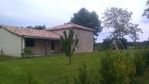 A two-story house with a tiled roof, a stone exterior, and a small front yard with a swing set.