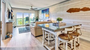 Une cuisine spacieuse avec une table à plateau en verre, des chaises en bois blanches et une décoration murale représentant des poissons en bois.