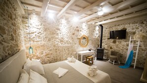 A cozy room with a stone wall, a bed with white linens, a wooden ceiling, a small table with a mirror, a TV mounted on the wall, and a chair. - Alice Residence - Two Storey Luxury Residence in the Heart of Rethymno Old Town (Rethymno)