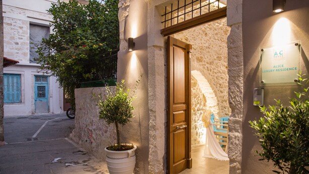 A narrow street with a building entrance, a potted tree, and a sign indicating "Alice Luxury Residence." - Alice Residence - Two Storey Luxury Residence in the Heart of Rethymno Old Town (Rethymno)