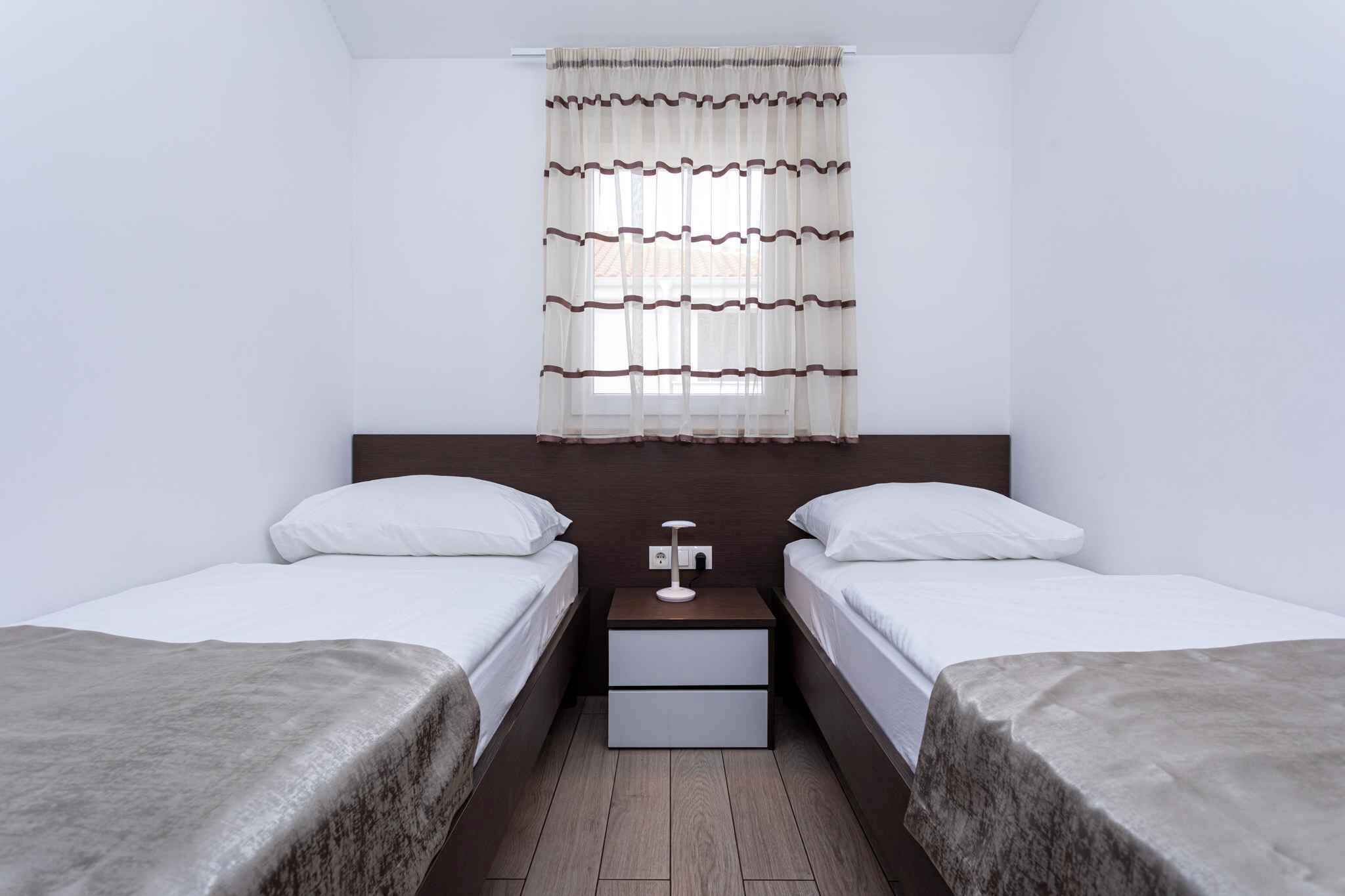 A hotel room with two single beds, a nightstand with a lamp, and a window with curtains.