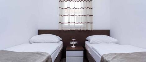 A hotel room with two single beds, a nightstand with a lamp, and a window with curtains.