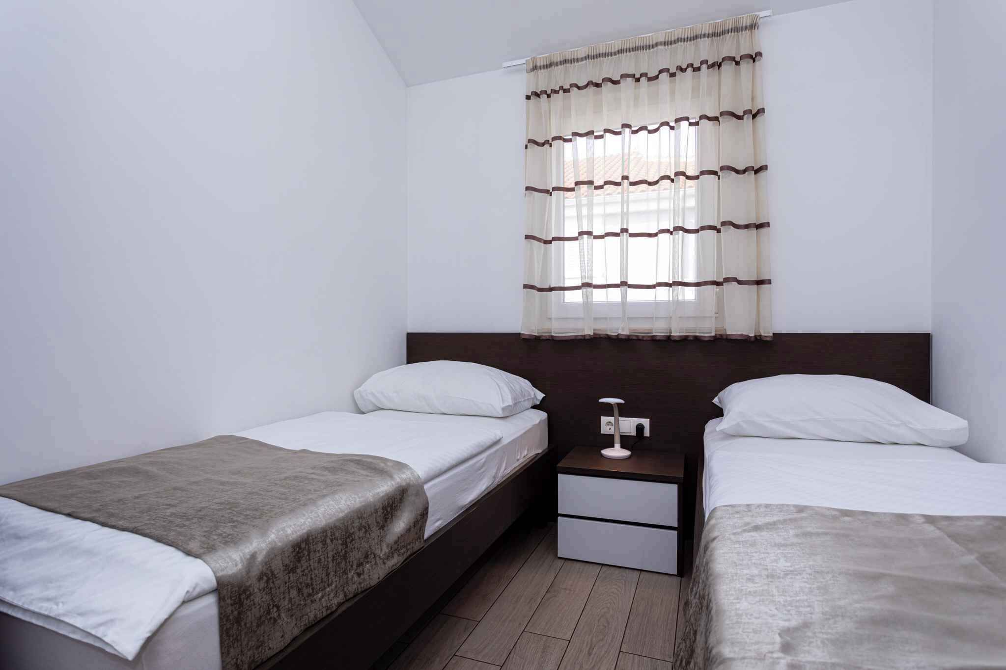 Une chambre d’hôtel avec deux lits simples, une table de chevet, une petite table et une fenêtre avec des rideaux.