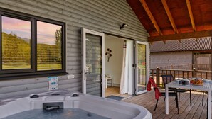 Een houten chalet met een jacuzzi, een tafel met buitenzitplaatsen en uitzicht op het omliggende landschap.