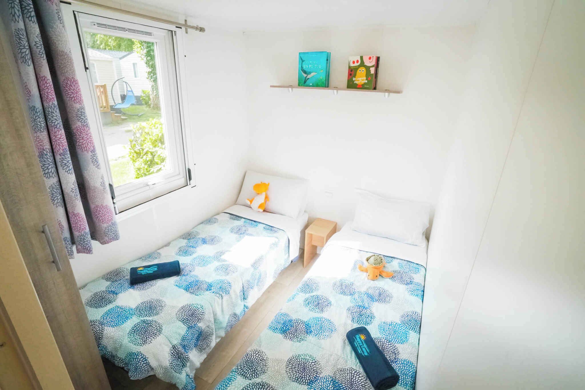 Ein kleines, kompaktes Zimmer mit zwei Einzelbetten, einem Fenster mit Vorhängen, einem Regal mit B üchern und einer Yogamatte auf dem Boden.
