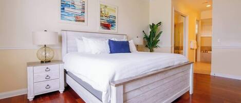 Une chambre à coucher avec un lit en bois, une literie blanche, une table de chevet avec une lampe et deux tableaux accrochés au mur.