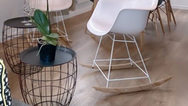 Een eetruimte met een tafel gedekt voor vier personen, omringd door moderne stoelen. Daarboven hangt een lamp en aan de muur hangt een schilderij.