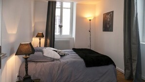 Een slaapkamer met een bed, twee bedlampen, een raam met gordijnen, een aan de muur hangend schilderij en een vloerkleed.