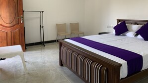 A neatly arranged bedroom with a wooden bed, a white bedside table, two chairs, and a door.