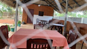A covered outdoor dining area with tables and chairs, a wooden door, and a thatched roof structure.