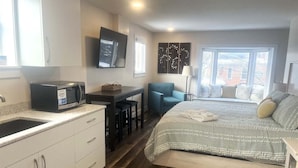 A bedroom with a bed, a desk, a chair, a TV, and a window. - Cozy 1-bedroom condo in downtown Saugatuck, perfect for a romantic getaway. (Saugatuck)