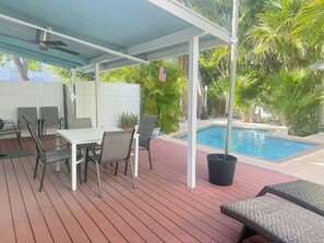 A covered outdoor area with a pool, a table with chairs, and potted plants. - Casa Rosa: 4BR/4BA house, pool, near Duval (Key West)