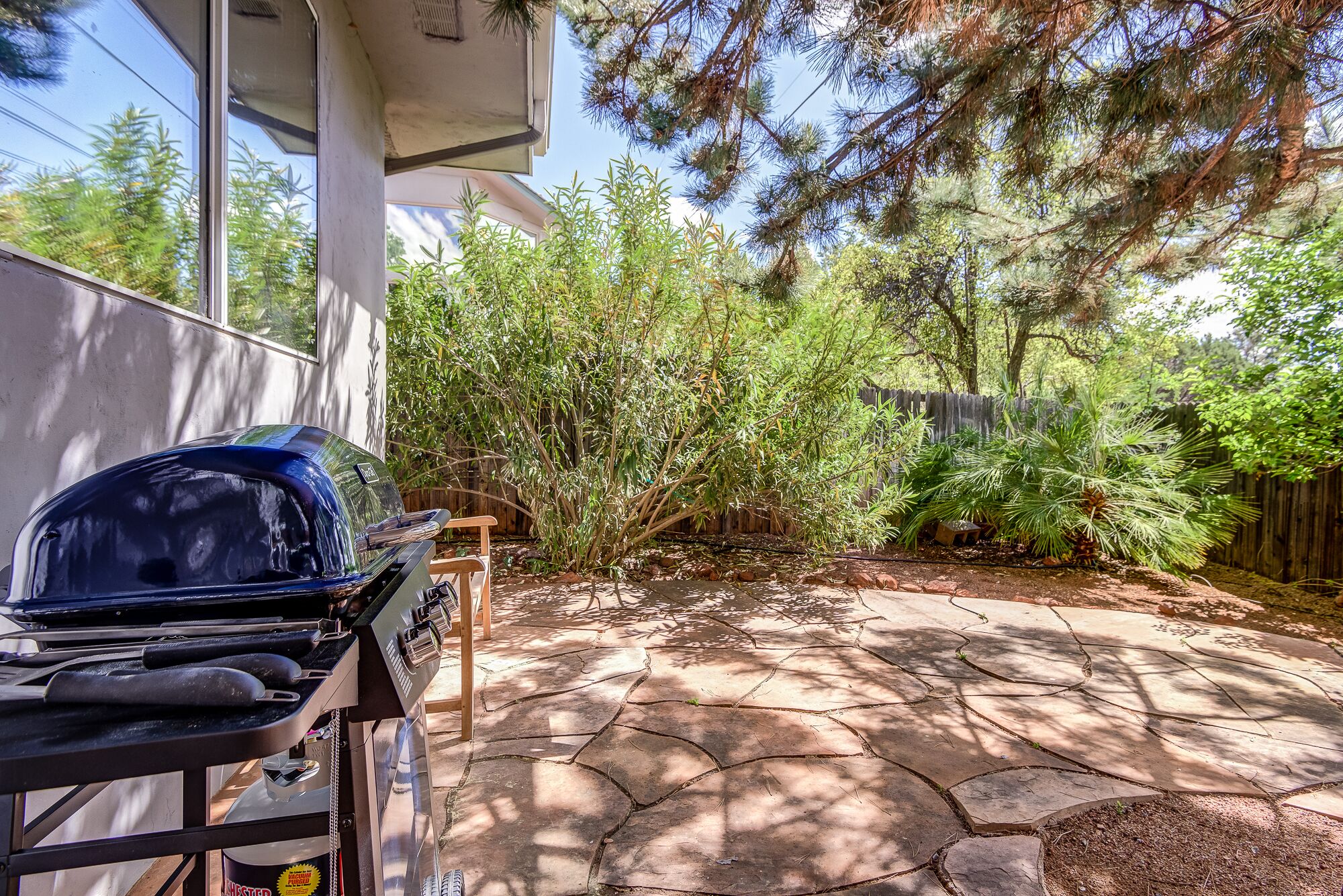 A patio with a barbecue grill, stone flooring, and a wooden fence.