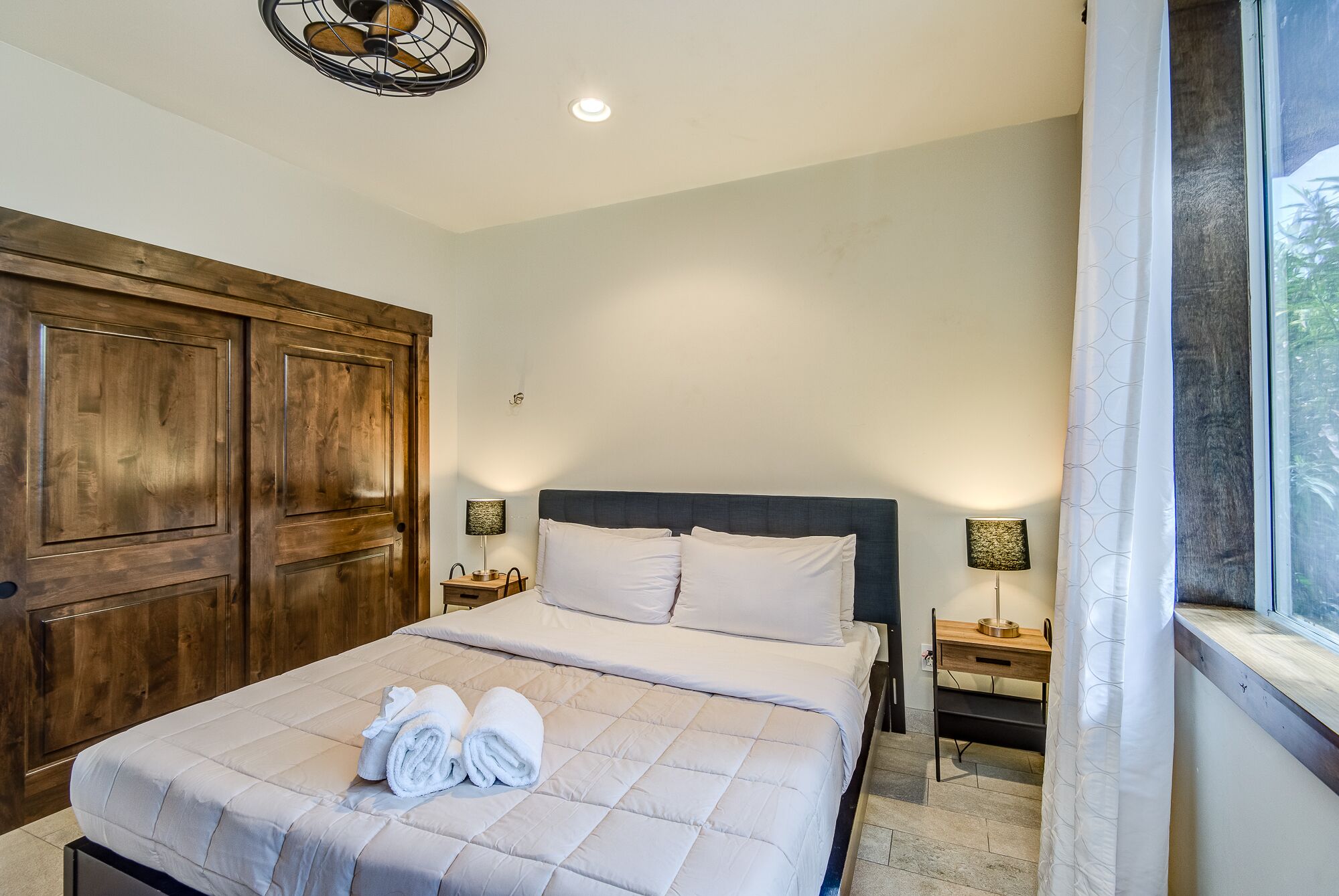 Een slaapkamer met een groot bed, een houten garderobe, twee nachtkastjes met lampen, en een raam met uitzicht.