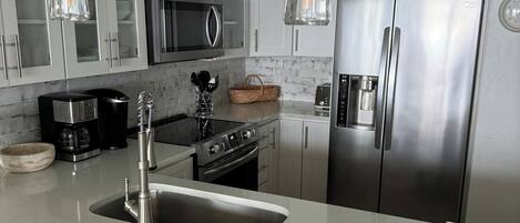 A modern kitchen with stainless steel appliances, a large island with a sink, and pendant lighting.